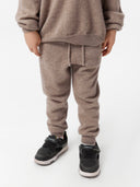 Person wearing a brown tracksuit with black shoes on a white background. #color_taupe