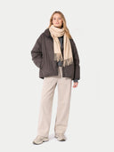 Woman wearing a dark jacket, beige scarf, and light pants on a white background #color_beige