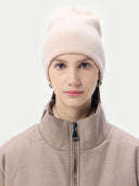 Person wearing a light pink knit beanie and beige jacket on a white background. #color_sand-beige