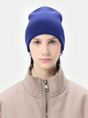 Person wearing a blue knit beanie and beige jacket on a white background. #color_deep-cobalt