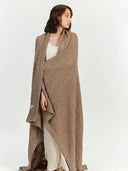 Woman wearing a brown cable knit shawl over a white outfit on a white background. #color_taupe