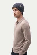 A man in profile wearing a dark gray ribbed knit beanie with a small white logo patch and a light brown long-sleeve polo shirt, set against a solid light gray background. #color_charcoal #ai-image