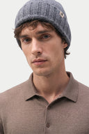 A close-up of a man wearing a gray ribbed knit beanie with a small woven logo patch and a brown polo shirt, against a plain light background. #color_charcoal #ai-image