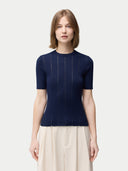 A woman wearing a navy blue ajour-knit cashmere silk top with short sleeves, paired with a light-colored skirt. #color_mood-indigo