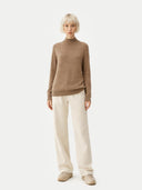 Person wearing a brown sweater and white pants on a white background Gobi Cashmere #color_taupe #ai-image