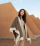Model wearing a brown and cream natural colour cashmere cape over a beige jumper and trousers, outdoors