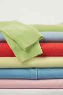 Folded jumpers in cashmere seasonal shades of green, blue, red, yellow and pink, stacked flat lay with ribbed cuff detail