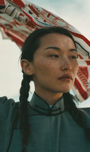 Model with braids in grey Mongolian collared garment under red patterned textile, marking the GOBI Cashmere rebrand