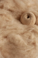 Ball of camel-toned yarn resting on raw Mongolian cashmere fibre, close-up detail view