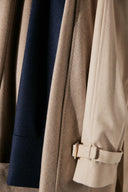 Close-up of cashmere coats in navy, taupe and cream, showing cuff strap with buckle detail