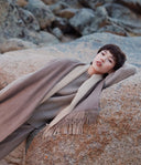 Model resting on rocks in beige and brown fringed scarf, showing Mongolian cashmere craftsmanship