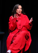 Celebrities wearing cashmere: Robin Thede seated on stage in a red double-breasted long coat, front view