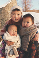 Three children outdoors in snow wrapped in Mongolian cashmere scarves and a ribbed beanie, winter portrait