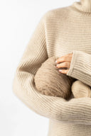 Model in beige ribbed roll neck jumper holding yarn skeins, showing how to get static out of cashmere