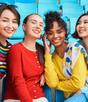 Four models in a colourful cashmere collection, striped, red buttoned and yellow jumpers on blue stadium seats