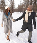 Couple walking in snow showing winter fashion trends, grey belted coat and dark lapel coat with scarf