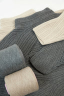 Health benefits of cashmere shown in ribbed grey and cream knits with two yarn cones, flat lay detail