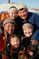 Smiling herder family in traditional deels and beige knitted hats outside a ger, Mongolian cashmere production heritage