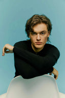 Model wearing a black men's cashmere jumper with crew neck, seated against a blue background, front view