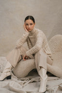 Model in beige patterned roll-neck jumper and trousers showing old money cashmere style, seated front view