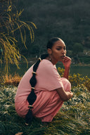Model crouching outdoors in pink ribbed short-sleeve top and trousers, lightweight cashmere wardrobe essentials, side view