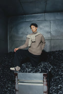 Model in beige textured knit jumper and scarf from the Pre-Fall 2025 cashmere collection, seated, front view