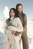 Two models in snow wearing the undyed cashmere collection, cream cable scarf, beige and brown knitwear with gloves