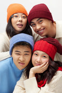 Four models wearing cashmere accessories, ribbed beanies in orange, burgundy, blue and red, close-up group view