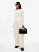 Person wearing a white outfit holding a black handbag on a white background. #color_white