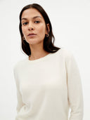 Woman wearing a white sweater against a plain background. #color_white