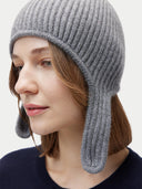 Woman wearing a gray knit hat with ear flaps on a light gray background