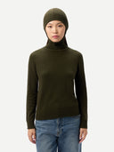 Person wearing a green turtleneck sweater and beanie with blue jeans on a white background