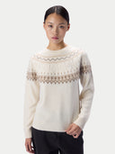 A model wearing a cream-colored knit sweater with a brown and beige Fair Isle pattern across the yoke and shoulders, paired with black pants, against a light gray studio background.