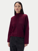 A woman modeling a cropped, long-sleeve knit top in deep burgundy with a central braided detail, paired with black pants, against a light gray studio background.