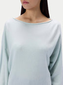 A close-up of a model wearing a pale mint green knit top with a wide boat neckline and long sleeves, set against a plain light background.