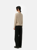Person wearing a beige sweater and black pants on a white background. #color_soft-beige