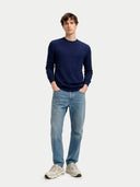 Man wearing a navy sweater and light blue jeans on a white background. #color_dark-indigo #ai-image
