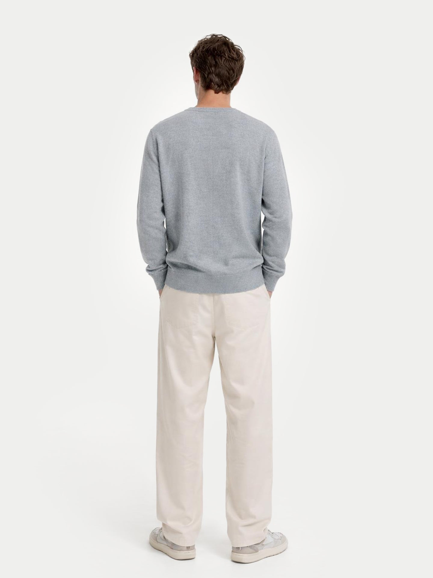 Man wearing a gray sweater and beige pants on a white background