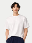 Person wearing a plain white t-shirt and dark pants on a light gray background. #color_ink-blue #ai-image