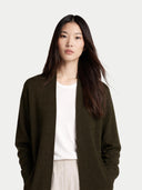 Woman wearing a dark green coat over a white shirt on a plain background #color_olive-green