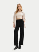 Woman wearing a beige top, black pants, and black boots on a white background. #color_off-white #ai-image