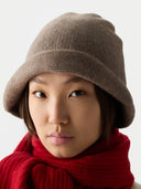 Person wearing a brown knitted hat and red scarf against a white background #color_taupe
