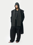 Person wearing a dark gray outfit with a hood on a white background
