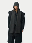 Person wearing a long black coat and gray hooded scarf on a white background