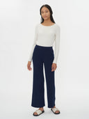 Woman wearing a white long-sleeve top and navy wide-leg pants on a white background. #color_navy-blue