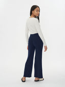 back view of a woman wearing a white top and navy pants on a white background. #color_navy-blue