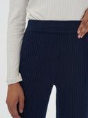 Navy ribbed pants worn with a light-colored sweater on a white background. #color_navy-blue