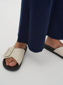 Beige sandals with black soles worn with navy pants on a white background. #color_navy-blue