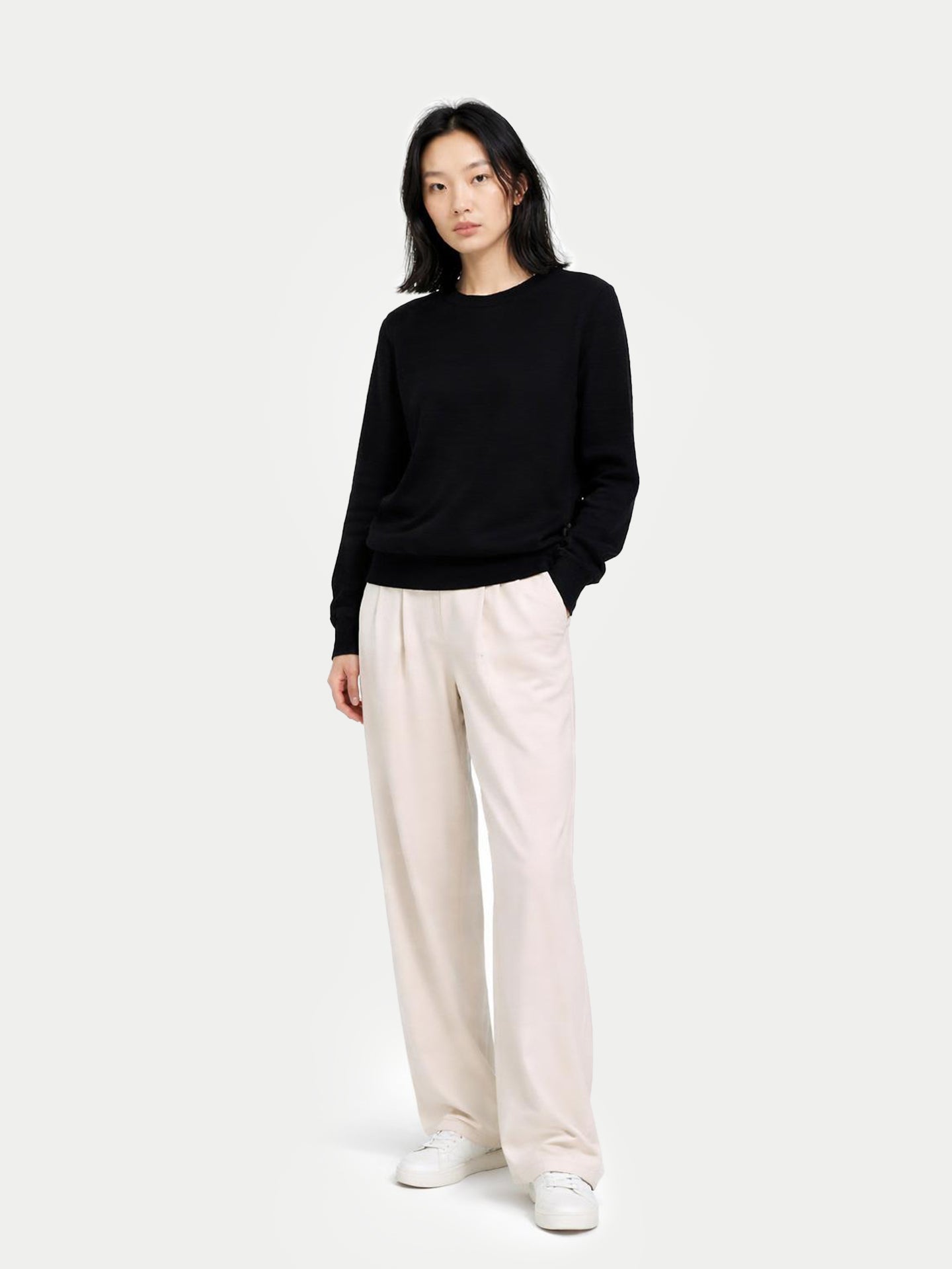Person wearing a black sweater and white pants on a white background