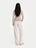 Woman wearing a beige long-sleeve top and light-colored pants on a white background